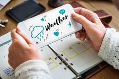 a person holding a planner with the word weather written on it, while sitting at a desk