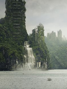 a large waterfall in the middle of a lake surrounded by tall buildings and forest on both sides