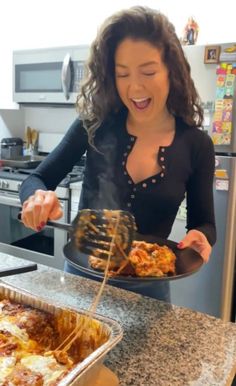 a woman holding a plate with food on it in front of a stove top oven