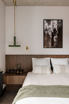 a bed with white sheets and pillows next to a painting on the wall above it