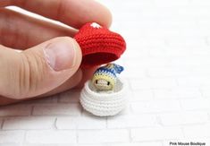 a hand holding a tiny crocheted toy with a stuffed animal in it