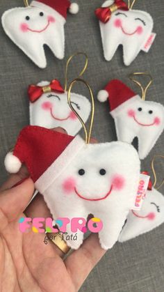 tooth shaped ornaments are being held up by someone's hand with santa hats on them