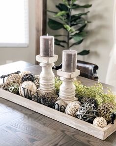 two candles sitting on top of a wooden tray filled with plants