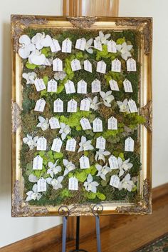 a moss covered wall with white flowers and small houses on it, sitting in front of a mirror