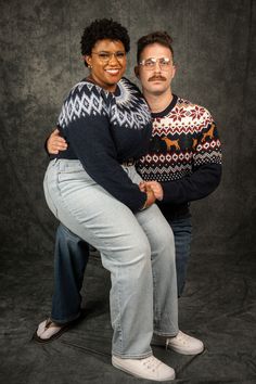 two people posing for a photo in front of a black background, one holding the other's back