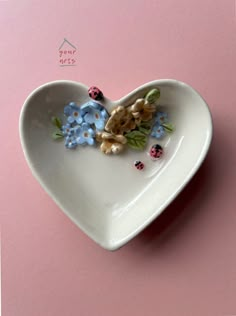 a white heart shaped dish with blue flowers and ladybugs on the side, against a pink background