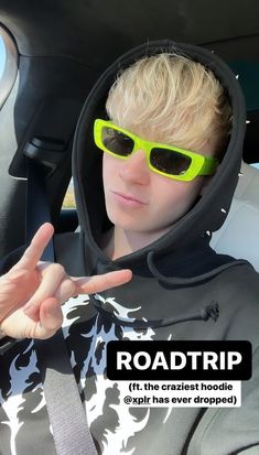 a young man wearing sunglasses sitting in the back seat of a car with his hand up