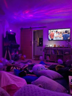 a living room filled with lots of pillows and purple lights on the ceiling, while people are watching tv