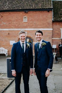 two men standing next to each other in front of a red brick building wearing suits and ties