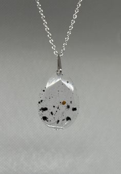 a necklace with black and white speckles hanging from it's side on a silver chain