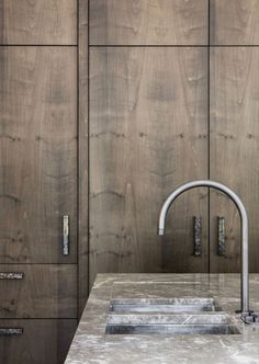 an image of a kitchen sink with faucets on the counter top and wood cabinets behind it