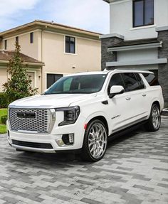 a white suv is parked in front of a house on a cobblestone driveway