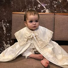 a baby sitting on top of a chair wearing a white dress