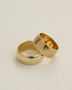 two gold wedding rings sitting next to each other on a white surface with no background