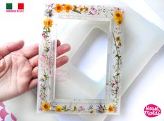 a hand holding a small white frame with flowers on it