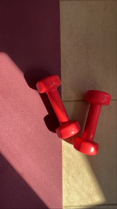 two red dumbs are on the floor next to a pink and beige wall with a shadow