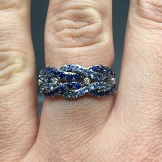 14K Sapphire and Diamond Band METAL: 14K White Gold TOTAL WEIGHT: DIAMONDS: 4 Round Brilliant Diamonds COLOR: G/H CLARITY: VS2 TOTAL WEIGHT: 0.04 ct GEMSTONES: Round brilliant cut blue sapphires TOTAL WEIGHT: 1.22 ct SIZE: Ladies size 5-8. Please indicate your ring size at checkout. DESCRIPTION: This gorgeous ring has a braided design of light and dark blue sapphires. It has four small bezel set diamonds in between each braid. It is 8.5mm wide with a 3mm height. The shank tapers down to 3mm. FRE Multi-stone Sapphire Promise Ring, Fine Jewelry Multi-stone Sapphire Promise Ring, Platinum Sapphire Multi-stone Jewelry, Sapphire Diamond-cut Round Band Jewelry, Sapphire Diamond Cut Round Band Jewelry, Sapphire Jewelry With Diamond Cut In Round Band, Anniversary Sapphire Diamond Ring With Multi-stones, Dazzling Multi-stone Sapphire Jewelry, Anniversary Multi-stone Sapphire Ring In White Gold