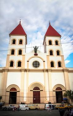 a large white church with red roof and two towers on the front, surrounded by parked cars