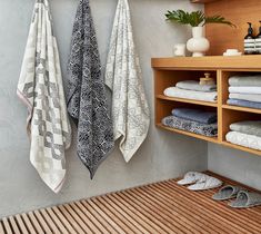 three towels hanging on the wall next to wooden shelves with shoes and slippers in them