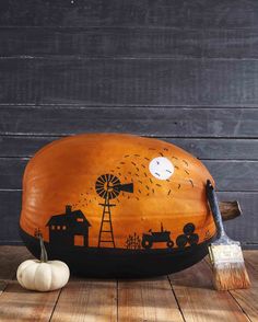 a pumpkin painted with an image of a farm and windmill is sitting on a wooden table