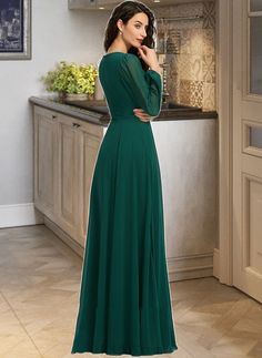 a woman standing in a kitchen wearing a long green dress with sleeves on the back