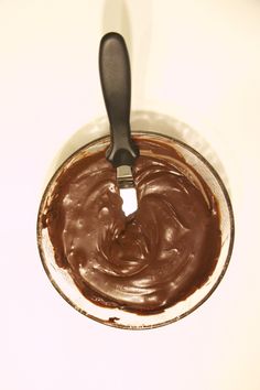 a spoon in a glass bowl filled with chocolate frosting on top of a white table