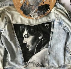 the back of a jean jacket with an image of a man's face painted on it