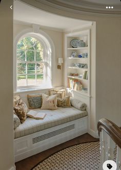 a window seat with pillows on it in front of a bookshelf