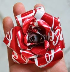 a hand holding a red and white lollipop candy flower with coca - cola on it