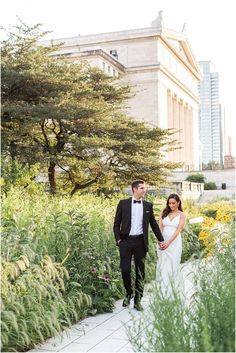 a bride and groom walking through the gardens at their wedding