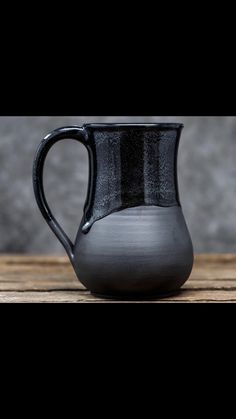 a black ceramic pitcher sitting on top of a wooden table next to a gray wall