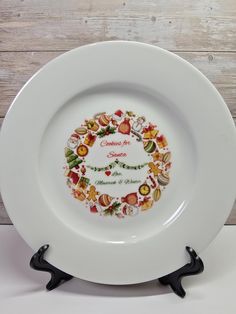 a white plate with a christmas wreath design on the front and bottom, sitting on a black stand