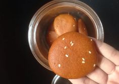 a hand holding a bun with sesame seeds on it in a glass container filled with water