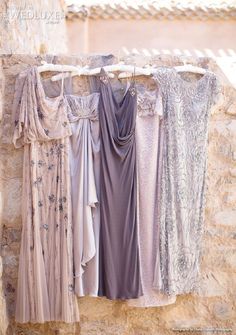 four dresses hanging on a clothes line in front of a stone wall with an open window