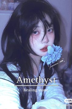 a woman with long black hair holding a blue flower in her mouth and looking at the camera