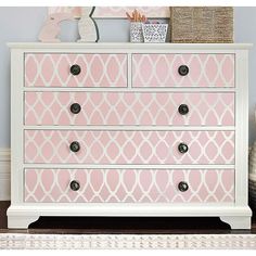 a pink and white dresser sitting on top of a wooden floor next to a wall