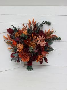 a bridal bouquet with orange and red flowers on a white wooden wall in front of a door