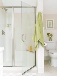 a bathroom with a glass shower door, toilet and green towel hanging on the wall