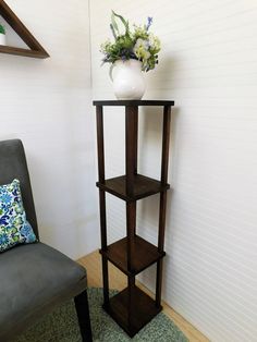 a corner shelf with a vase and flowers on it next to a gray chair in a living room