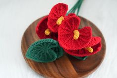 two crocheted red flowers sitting on top of a wooden plate