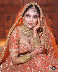 a woman in an orange and gold bridal outfit posing for the camera with her hands on her face