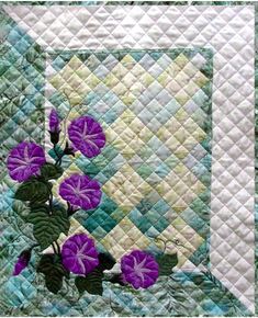 a quilted wall hanging with blue flowers on it's side and green leaves in the center