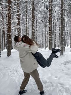 a man carrying a woman through the snow in front of some trees with no leaves