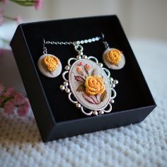 a necklace and earring set in a box on a table with flowers behind it