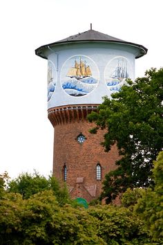 a water tower painted with pictures of ships on it's side and surrounded by trees