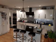 a kitchen with white cabinets and black counter tops is pictured in this image, there are three stools at the center of the island