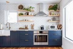 a kitchen with blue cabinets and white subway backsplash, wood flooring and open shelving