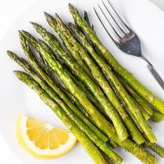 asparagus spears on a plate with lemon wedges and fork next to it