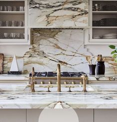 a kitchen with marble counter tops and gold faucets on the stove top, along with white cabinets