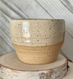 a white and brown bowl sitting on top of a piece of wood next to a tree stump